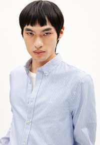 Blauw-wit gestreepte overhemd met knopen en een kraag, voorzien van een klein logo op de borst en een gladde stofstructuur.