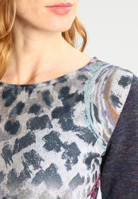 Haut à manches longues présentant un motif géométrique multicolore avec des accents d'imprimé animalier, fabriqué en tissu doux, mettant en valeur des textures et des nuances variées.