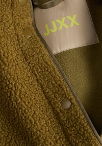 Καφέ υφασμάτινο fleece μπουφάν με κουμπιά και ετικέτα υφάσματος στο εσωτερικό που δείχνει πράσινο κείμενο "JJXX".
