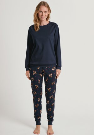 Dunkelblaues Sweatshirt mit langen Ärmeln, kombiniert mit gemusterten Schlafanzughosen, die orangefarbene Reh- und Herzmotive aufweisen. Weicher Stoff, lässiger Schnitt.