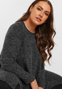 Wielki sweter w kolorze węglenowo-szarym, wykonany z teksturowanej dzianiny, z okrągłym dekoltem i długimi rękawami oraz luźnym wykończeniem.