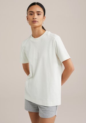 Lysebeige kortærmet t-shirt i blødt, glat materiale med rund halsudskæring og minimale sømme, parret med grå shorts.