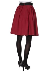 Gonna a metà lunghezza bordeaux con pieghe, cintura nera e zip sul retro. Indossata con collant neri e scarpe con tacco alto.