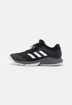 Chaussure de sport basse noire avec des rayures blanches, une semelle intermédiaire grise et une semelle extérieure blanche, avec des lacets noirs et une tige en mesh pour la ventilation.