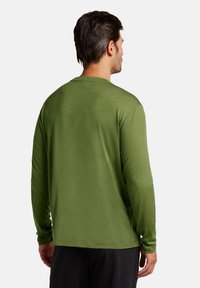 Långärmad T-shirt i olivgrön, tillverkad av texturerat tyg, har en avslappnad passform och rundad halsringning. Visad från baksidan.