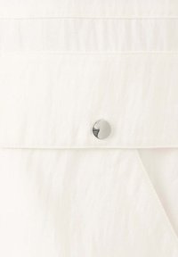 Gros plan sur un tissu blanc avec un bouton-pression métallique sur une couture de vêtement.