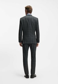 Abito a scacchi grigio scuro con una vestibilità su misura, caratterizzato da uno spacco singolo e tasche inclinate. Abbinato a scarpe nere e una camicia azzurro chiaro.