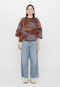 Mönstrad färgglad tröja med puffärmar, brun halsringning; kombinerad med vida ljusblå jeans och vita sneakers. Brun crossbody-väska.