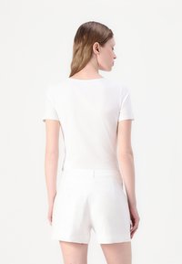 Camiseta blanca de manga corta con cuello redondo combinada con pantalones cortos blancos. La tela parece suave y ligera con una silueta ajustada.
