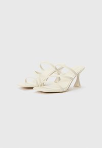Strappy sandals with a clear heel, made of a smooth, off-white material. Features multiple thin straps and a square toe design.
