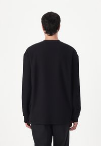 Pull-over noir à manches longues avec une coupe décontractée, texture côtelée, encolure ras du cou et épaule tombante. Détails de couture visibles aux coutures.