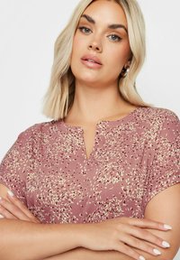 Blusa a maniche corte color lampone con scollatura a V, caratterizzata da un motivo maculato in crema e borgogna scuro. Tessuto morbido e strutturato.