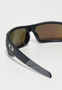 Schwarze Sonnenbrille mit dunklen Gläsern, solidem Rahmen und strukturierten grauen Akzenten an den Bügeln mit diagonalen Streifen.