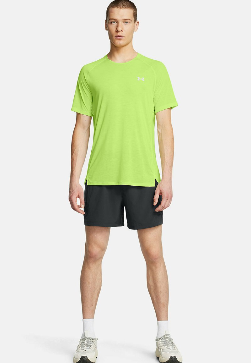 T-shirt de sport à manches courtes vert vif en tissu évacuant l'humidité, associé à un short noir. Présente un logo sur la poitrine et une coupe décontractée.