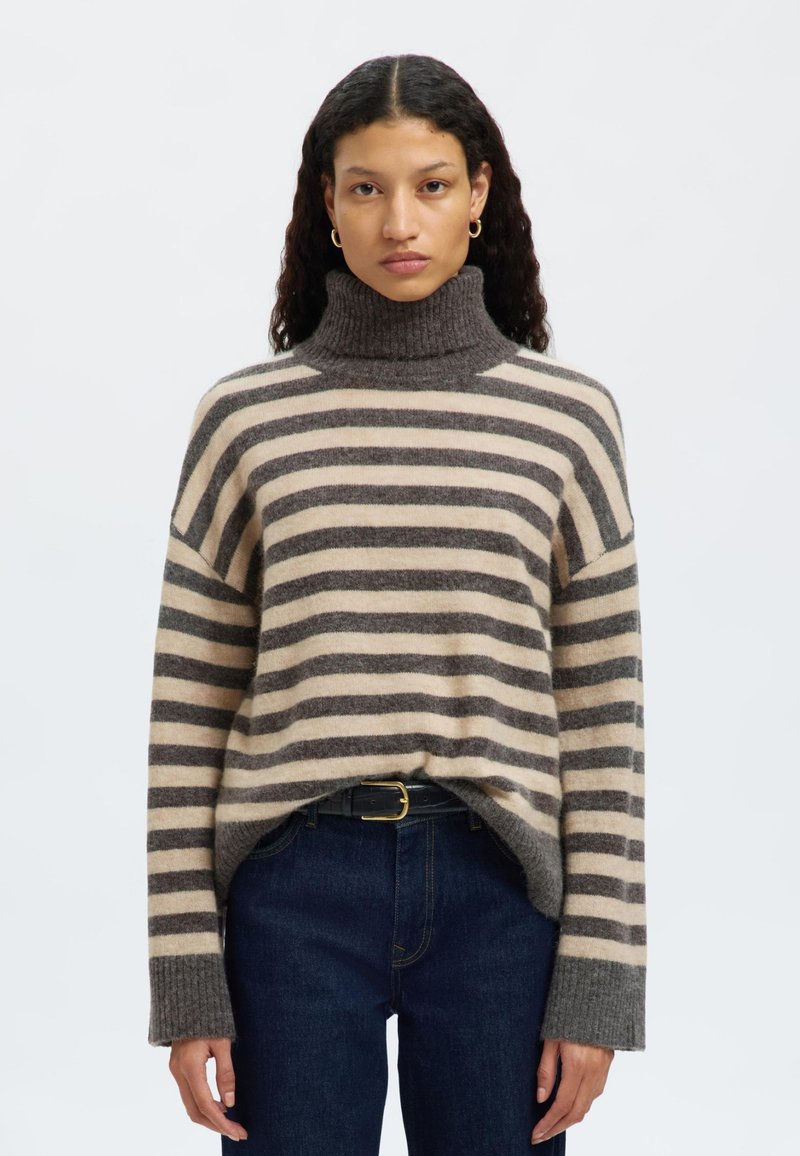 Csíkos kötött pulóver bézs és szürke színekben, magas garbónyakkal, lógó vállakkal és bordás mandzsettákkal. Sötétkék farmer felett viselve.