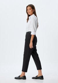 Camicia bianca con bottoni, pantaloni neri a vita alta, mocassini neri e una cintura nera sottile. Tessuto liscio con vestibilità su misura.