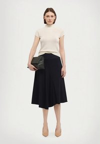 Beigeä ribbineulosta lyhythihainen toppi, yhdistetty tummansiniseen A-linjamekkoon. Malli pitää kädessään mustaa clutch-laukkua ja pukeutunut nudenvärisiin korkeakorkoisiin kenkiin. Yksinkertainen muotoilu.