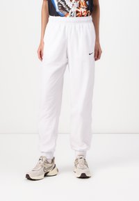 Jogging blancs en tissu léger, dotés d'une taille élastique et de poignets aux chevilles, avec un petit logo Nike noir sur le côté.