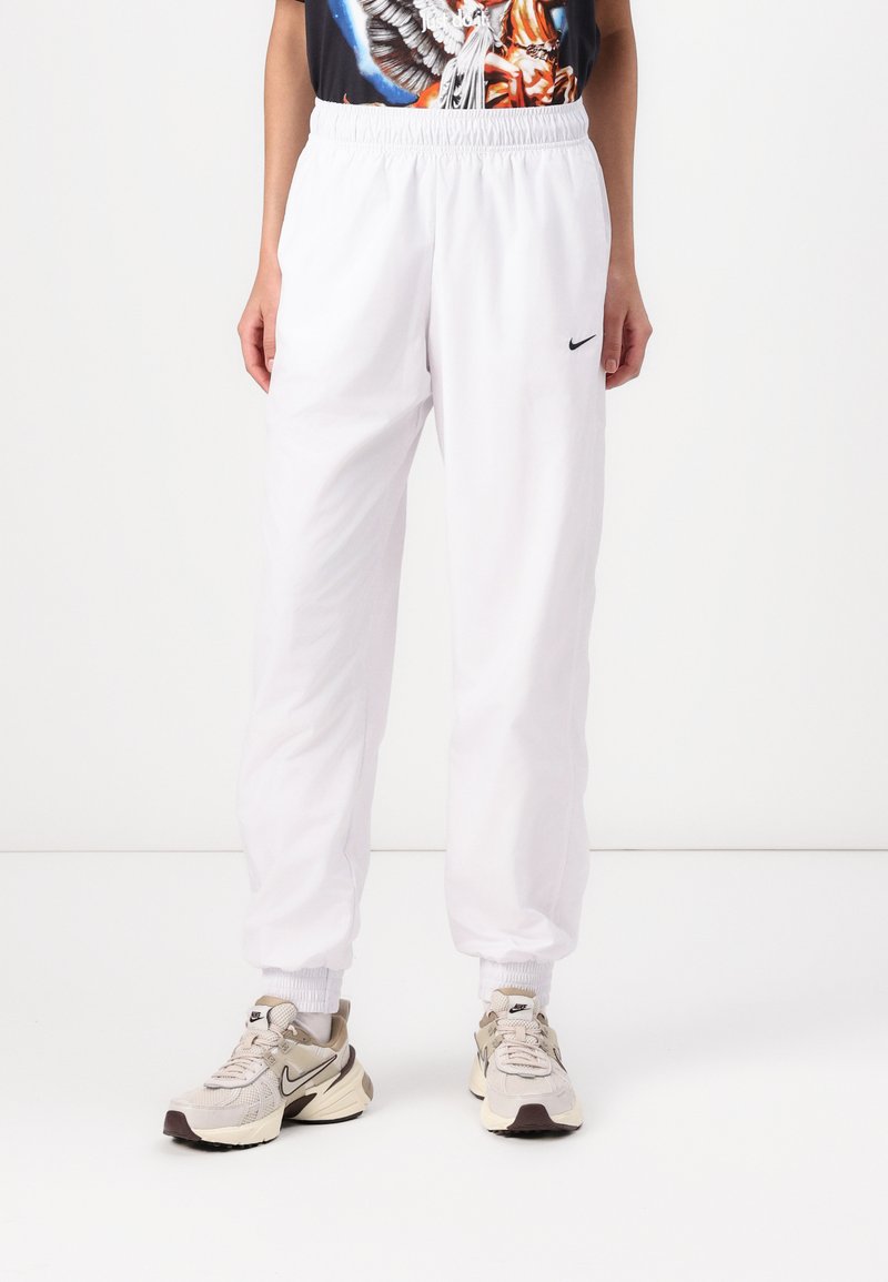 Jogging blancs en tissu léger, dotés d'une taille élastique et de poignets aux chevilles, avec un petit logo Nike noir sur le côté.
