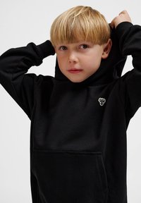 Schwarzer Kapuzenpullover aus weichem Stoff mit einer vorderen Tasche, der ein kleines grafisches Detail auf der Brust aufweist. Schlichtes, lässiges Design mit Kapuze.