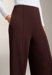 Bordowe spodnie o szerokich nogawkach z gładką fakturą, z pionowymi szwami i bocznymi kieszeniami. Wykonane z elastycznego materiału dla wygody.