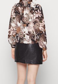 Blusa a maniche lunghe con un motivo floreale nei toni del rosa, marrone e verde; abbinata a una mini gonna in pelle nera. Tessuto testurizzato, vestibilità comoda.