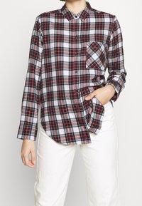Rood, zwart en witte geruite button-up shirt met een kraag, lange mouwen en een enkele borstzak, gecombineerd met witte broek. Van katoen.