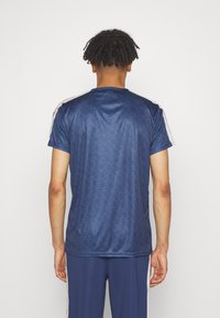 Granatowa koszulka sportowa z geometrycznym wzorem, krótki rękaw i kontrastowe białe paski na ramionach, wykonana z gładkiego, lekkiego materiału.