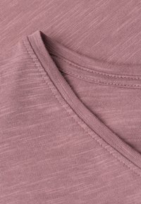 Gros plan d’un tissu mauve montrant des coutures détaillées le long d’une couture pliée, mettant en valeur la texture et le motif tricoté.