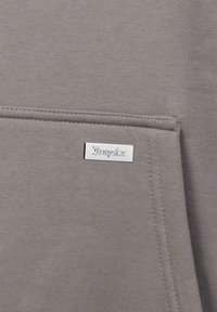 Grauer Sweatshirtstoff mit einer glatten Textur, mit einem kleinen silbernen Etikett mit der Aufschrift "Dropside" und einem Detail mit einer Fronttasche.