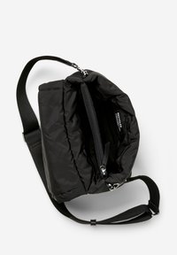 Černá polstrovaná crossbody taška s nastavitelným popruhem, otevřenou hlavní kapsou, viditelnou vnitřní zipovou kapsou a štítkem "Recyklováno" uvnitř.