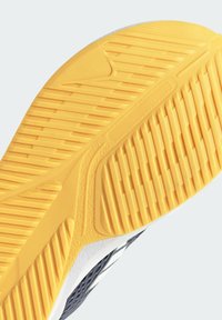 Suela de zapato con un fondo de goma amarilla texturada, con surcos y crestas, diseñado para tracción, junto a un borde superior en blanco y negro.