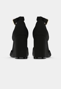 Svarta högklackade skor med en slät, matt tygfinish. Har en vristrem med ett guldspänne och en klumpig klackdesign.