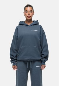 Felpa oversize blu scuro con tasca a marsupio e cappuccio con cordino, con la scritta bianca "GOODFORNOTHING" sul petto e pantaloni della tuta coordinati.