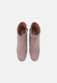 Botines de ante en un suave color malva, con una textura lisa, punta redondeada y un cierre de cremallera lateral para facilitar su uso.