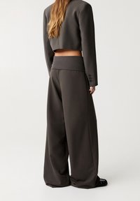 Bruine, wijde broek met een zachte tailleband, gecombineerd met een cropped, nauwsluitend jasje met knoopdetails. Glad stoffen textuur.