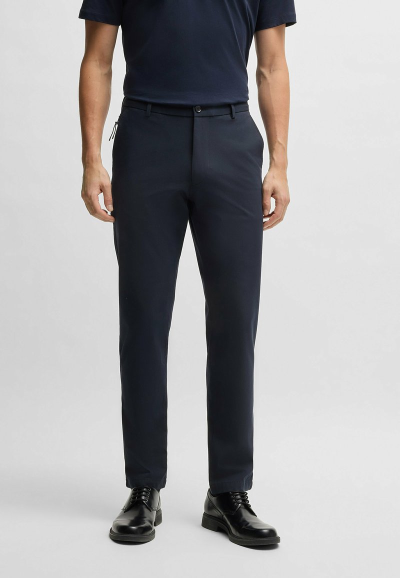 Dark navy tailored pants made of smooth fabric, featuring a button closure, side pockets, and a slim fit. Worn with black dress shoes.
