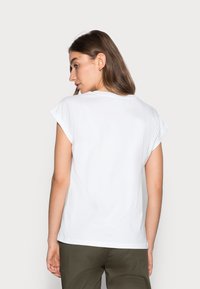 Camiseta blanca con mangas cortas enrolladas, material de algodón suave, diseño de cuello redondo, textura lisa y estilo minimalista.