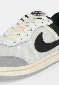 Бяла и сива маратонка Nike Air с черно лого swoosh, кремави връзки и горна част от текстурирана материя отблизо.