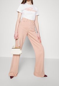 Light pink wide-leg trousers with a high waist, paired with a white T-shirt featuring a colorful logo. A small white handbag is held.