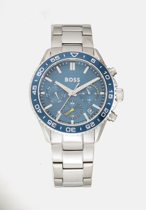 Montre en acier inoxydable argenté avec un cadran bleu, des aiguilles luminescentes et des sous-cadrans. Dispose d'une lunette tournante bleue et d'une fenêtre de date à 4 heures.