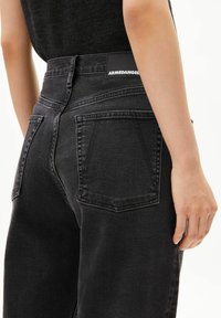 Jean denim noir à taille haute et jambes droites, avec des poches arrière et une étiquette en cuir portant le logo sur la ceinture.