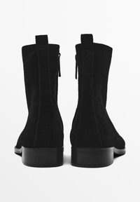 Bottines noires en suede avec un talon épais, dotées d'une fermeture éclair et d'un tirant à l'arrière, surface supérieure lisse et design épuré.