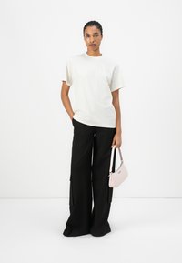 Cream cotton T-shirt with a round neck, paired with black wide-leg trousers featuring cargo pockets and a small pink shoulder bag.