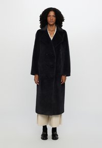 Long, dark navy coat made of soft, textured fabric. Features a double-breasted design with large black buttons and a wide collar.
