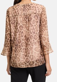 Blus med leopardtryck och utställda ärmar, tillverkad av genomskinligt tyg. Har en rundad halsringning och en plisserad bakdesign i varma beige toner.