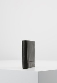 Schwarze Lederbörse mit strukturiertem Finish, rechteckiger Form und sichtbaren Nähten entlang des Randes. Allein auf einer hellen Oberfläche.