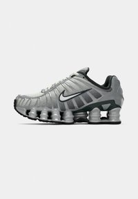 Szare i czarne buty biegowe Nike z widocznym, sprężystym tłumieniem pod podeszwą oraz białym logo swoosh po boku.