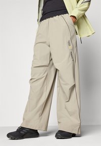 Beige, lette bukser med løs passform, aksentert med svart piping og merkelapper. Har en elastisk midje for komfort.