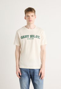 Cream-colored cotton t-shirt featuring a green printed text "GANT NH. CT. SPORTS CLUB," short sleeves, and a classic crew neck design.